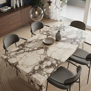 May include: A contemporary dining set with a rectangular table featuring a marble-effect top and dark grey chairs. The table is set with plates and a vase of greenery. The room has a neutral colour palette with wooden flooring and a woven rug.