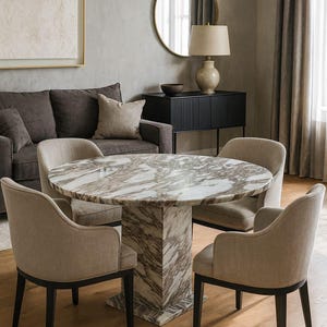 Op de afbeelding: Een moderne eethoek met een ronde tafel met marmeren blad, ondersteund door een patroonvoet, en vier gestoffeerde stoelen met donkere houten poten. De kamer omvat ook een bank, een bijzettafel en een ronde spiegel.