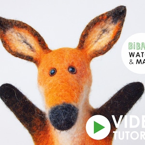 Op de afbeelding: Een handgemaakte oranje vos van vilt met zwarte accenten. De vos heeft grote oren, blauwe ogen en uitgestrekte armen. De afbeelding bevat de tekst "BiBaBo Watch & Make" en een video tutorial knop.