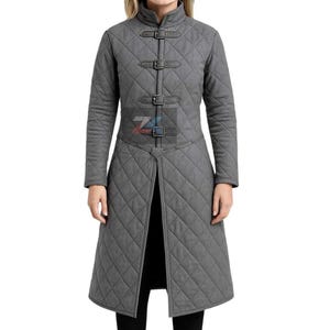 May include: A gray quilted coat with a high collar and long sleeves. The coat features three leather buckle closures down the front and a split hem. The coat is a mid-length design, suitable for cooler weather.