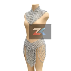 Peut inclure: Ensemble haut et jupe en cotte de mailles argentée présenté sur un mannequin. Le haut est un col montant, et la jupe présente un design en chaîne drapée. L'ensemble est fait de petits anneaux métalliques.