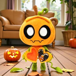 May include: A plush pumpkin-headed character with large white eyes and a stitched smile. It holds a heart-shaped accessory and has green limbs. A carved pumpkin and fall leaves are nearby, suggesting a Halloween theme.