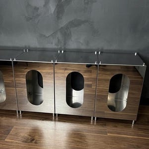 May include: A set of modern pet furniture with a wood grain finish and stainless steel accents. Each unit features an oval opening and sits on short, silver legs. The units are arranged in a row, with a dark gray wall in the background.