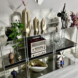 May include: A mirrored shelving unit showcases various decorative items. Beige vases, a silver elephant statue, and a vintage radio are displayed. A glass bowl and a small windmill figurine are also visible. The unit is against a white wall.