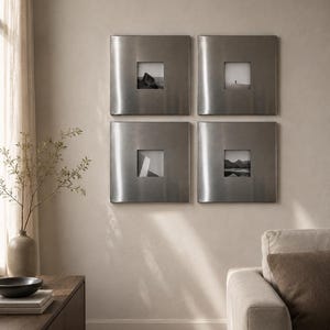 Op de afbeelding: Vier vierkante wandlijsten met een geborstelde zilverkleurige metalen afwerking, elk met een gecentreerde vierkante zwart-witfoto. De lijsten zijn in een twee-bij-twee raster op een effen muur geplaatst en hebben een glad, reflecterend oppervlak.