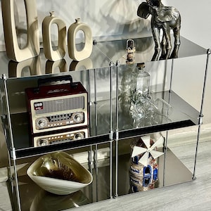 以下が含まれることがあります： クロムメッキの棚に装飾品が飾られています。上の棚にはブロンズの象の像と小さな置物があります。真ん中の棚にはヴィンテージラジオが置かれています。下の棚には装飾的なボウルと風車の置物があります。