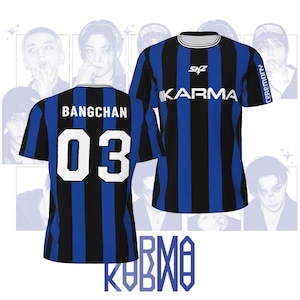 Puede incluir: Camiseta a rayas azules y negras con el nombre "BANGCHAN" y el número "03" en la espalda. La parte delantera de la camiseta tiene la palabra "KARMA" y las letras "SKZ". La camiseta tiene cuello y ribete blancos.