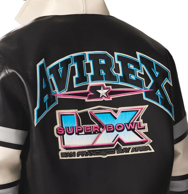 Puede incluir: Chaqueta de cuero negra con detalles en blanco y gris. La parte trasera presenta la palabra "AVIREX" en letras azules y rosas, junto con "SUPER BOWL LX" y "SAN FRANCISCO BAY AREA".