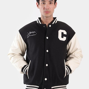 May include: Black varsity jacket with cream-colored sleeves and a white "C" patch. The jacket features white stripes on the cuffs and hem, and the text "Athletic Division" is written on the chest.