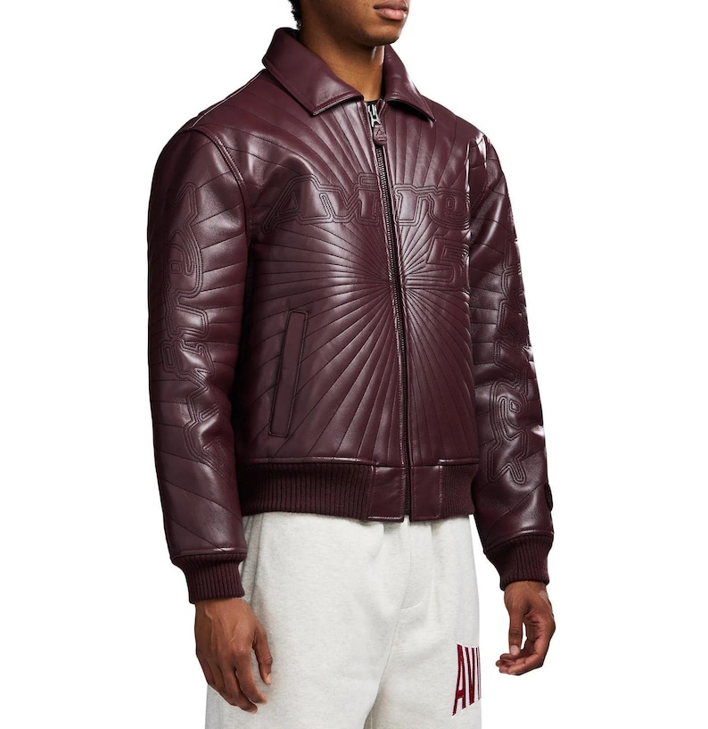 May include: A burgundy leather jacket with a zip-up front, a collar, and a ribbed hem and cuffs. The jacket features a sunburst design and the word "AMIRI" stitched across the chest.