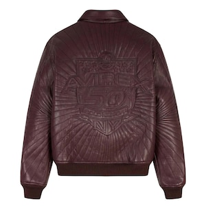 May include: A burgundy leather bomber jacket with a quilted design. The back features an embossed logo with the text "AVIREX 50 GOLD KICKOFF NY" in a sunburst pattern. The jacket has a ribbed hem and cuffs.
