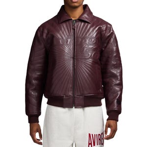 May include: A burgundy leather jacket with a zip-up front and a collar. The jacket features embossed text and a radial design on the front. The sleeves and back also have embossed designs. The jacket has ribbed cuffs and a waistband.