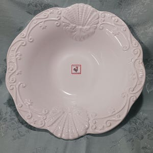 May include: White ceramic serving bowl with a scalloped edge and seashell and scrollwork detailing. The bowl has a smooth, glossy finish and a small sticker with a rooster logo. A decorative piece for serving food.