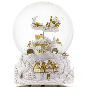 Peut inclure: Un globe de neige de Noël blanc et doré représentant le Père Noël dans un traîneau tiré par un renne au-dessus d'un village. La base est une montagne enneigée avec des maisons et des arbres détaillés.