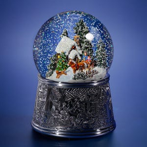 May include: A snow globe with a winter scene inside. The globe features a house, trees, and figures in a horse-drawn carriage. The base is silver with an embossed design. The globe is filled with water and glitter, creating a snowy effect.