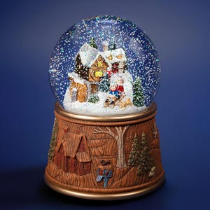 May include: A snow globe with a winter scene inside. The globe features a miniature village with houses, trees, and figures. The base is brown with carved winter scenes. The globe is filled with water and glitter.