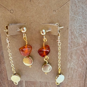 Può includere: Un paio di orecchini color oro con perno, una perla irregolare color ambra e un piccolo disco color oro. Ogni orecchino include anche una catenella color oro separata con un piccolo disco color oro all'estremità inferiore.