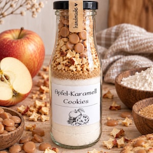 Könnte beinhalten: Eine klare Glasflasche gefüllt mit geschichteten trockenen Zutaten für Apfel-Karamell Cookies. Die Flasche hat einen schwarzen Deckel mit einem handmade-Etikett und ein weißes Etikett mit dem Text Apfel-Karamell Cookies und einer Apfelzeichnung.