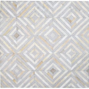Puede incluir: Una alfombra cuadrada con un patrón geométrico. La alfombra presenta un diseño repetitivo de diamantes y rayas diagonales en tonos grises, blancos y beige. La alfombra está hecha de un material texturizado, probablemente piel o cuero.