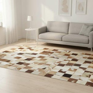 May include: A rectangular area rug with a patchwork design. The rug features squares of varying shades of brown, beige, and white. The rug is placed on a light-colored wooden floor in a living room setting.