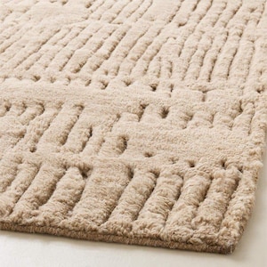 Könnte beinhalten: Ein beigefarbener Teppich mit einer strukturierten Oberfläche, die ein sich wiederholendes Muster aus erhabenen Linien und kleinen Löchern aufweist. Der Teppich hat ein weiches, plüschiges Aussehen mit subtilen Farbvariationen. Das Design erzeugt ein Gefühl von Tiefe und visuellem Interesse.