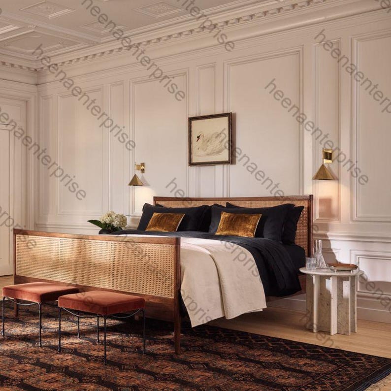 K&ouml;nnte beinhalten: Ein Schlafzimmer mit einem Holzbetttrahmen mit einem gewebten Kopf- und Fu&szlig;teil. Das Bett hat schwarze Bettw&auml;sche und goldfarbene Akzentkissen. Zwei kleine, rostfarbene Hocker stehen am Fu&szlig;ende des Bettes, und ein gemusterter Teppich bedeckt den Boden.