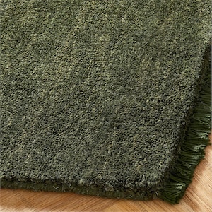 May include: Close-up of a green rug with a textured surface and fringe detail. The rug has a plush, dense pile, and the colour is a deep, earthy green. The fringe is a matching green colour.