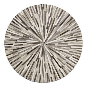 May include: A round rug with a radial design. The rug is made of rectangular pieces in shades of gray, black, and white, arranged to radiate from the center. The rug's pattern creates a starburst effect, suitable for home decor.