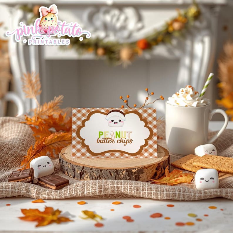 May include: A fall-themed image featuring a card that reads "PEANUT butter chips" with a cute cartoon peanut character. The card sits on a wooden slice, surrounded by marshmallows, chocolate, graham crackers, and a mug of whipped cream.