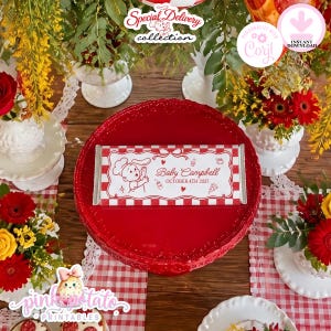 May include: A rectangular candy bar wrapper featuring a red and white checkered border, a central white panel with a cartoon chef, the text Baby Campbell, OCTOBER 4TH 2027, and small icons of a baby bottle, pacifier, and pizza slice.