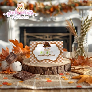 May include: A festive display featuring a card with the text "FLUFFY marshmallows" and a cartoon marshmallow wearing a pilgrim hat. The card sits on a wooden slice, surrounded by chocolate, marshmallows, and fall foliage. A jar with straws is in the background.