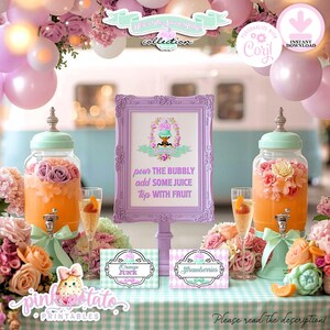 May include: A decorative party scene featuring two glass dispensers filled with orange liquid and floral arrangements. A framed sign reads "Pour the bubbly, add some juice, top with fruit." Additional signs indicate orange juice and strawberries. Pink and purple balloons decorate the background.