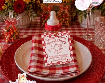 Pode incluir: Uma mamadeira com tampa vermelha e uma etiqueta branca com texto vermelho e um gráfico de bebê chef. A etiqueta diz Special Delivery, Thank you for showering Baby Campbell with love, Laura & Mark. A mamadeira está sobre um guardanapo xadrez vermelho e branco.