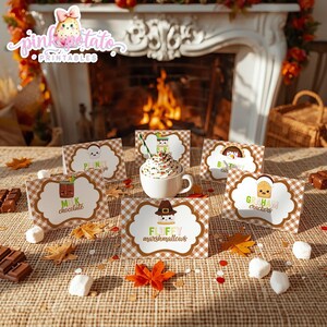 May include: A cozy scene featuring a mug of whipped cream-topped hot chocolate surrounded by ingredient cards for s'mores. The cards are labeled with text like "Fluffy Marshmallows" and "Graham Crackers" on a brown and white checkered background. Autumn leaves and chocolate bars complete the setting.