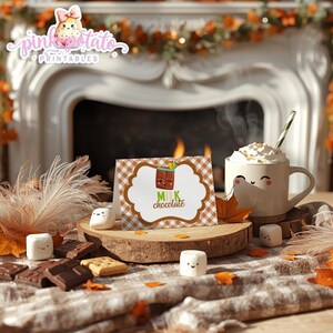 May include: A cozy scene featuring a mug of whipped cream-topped beverage, a card with a milk chocolate illustration, marshmallows, and chocolate bars. The card reads "Milk Chocolate" and is set against a fireplace backdrop with fall foliage.
