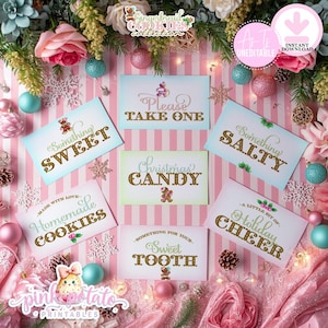 May include: A festive arrangement featuring cards with gold lettering and gingerbread man illustrations. The cards read "Something Sweet," "Please Take One," "Something Salty," "Christmas Candy," "Homemade Cookies," "Sweet Tooth," and "Holiday Cheer." Pink and blue ornaments and flowers surround the cards.