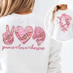 May include: White sweatshirt with a pink peace sign, heart, and horse graphic. The design includes floral and patchwork patterns, with the words "peace love horses" in pink script. A smaller image of a woman wearing a cowboy hat is on the right.