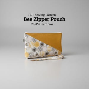 Könnte beinhalten: Eine rechteckige Reißverschlusstasche mit Bienenmotiv und einer Handschlaufe. Die Tasche hat ein diagonales Farbblockdesign mit Senfgelb und einem gemusterten Stoff mit Bienen und Waben. Der Text "Bee Zipper Pouch" ist sichtbar.