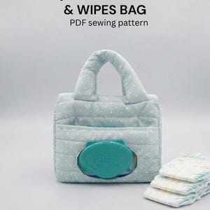May include: A light blue quilted diaper and wipes bag with white polka dots. The bag has a handle and a front pocket with a teal wipes container. The text "Quilted Diaper & Wipes Bag" is visible.