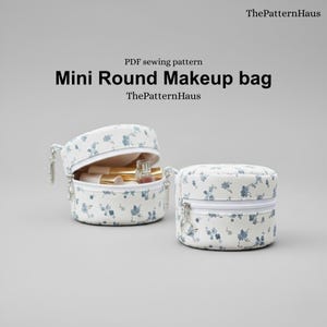 Pode incluir: Duas mini bolsas de maquiagem redondas com um padrão floral. Uma bolsa está aberta, revelando itens de maquiagem. As bolsas são brancas com um design floral azul e zíperes prateados. O texto na imagem diz "Mini Round Makeup bag".