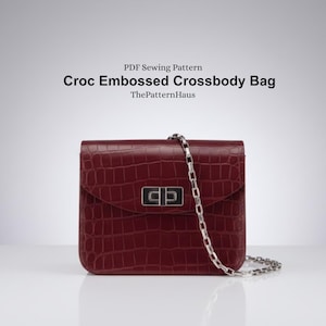 May include: A burgundy crossbody bag with a crocodile-embossed texture. It has a silver chain strap and a rectangular clasp. The text "Croc Embossed Crossbody Bag" is displayed above the bag.