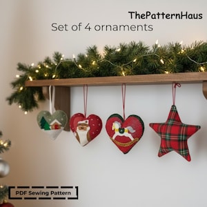 May include: Set of four handmade Christmas ornaments. Includes a green heart with a winter scene, two red heart ornaments with festive designs, and a red plaid star. The ornaments are hanging from a wooden shelf.