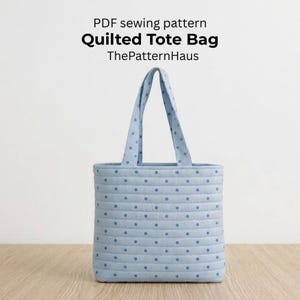 Może przedstawiać: Jasnoniebieska pikowana torba typu tote z niebieskimi kropkami. Torba ma dwa uchwyty i napis "PDF sewing pattern Quilted Tote Bag ThePatternHaus". Torba jest wykonana z miękkiej, pikowanej tkaniny.