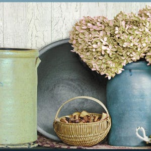 May include: A rustic still life featuring antique stoneware crocks with blue floral designs, a lit candle, a small woven basket, and a blue vase filled with dried flowers. The scene evokes a vintage, farmhouse aesthetic.