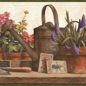 May include: A rustic brown watering can and a terracotta pot with purple flowers sit on a wooden surface. Two seed packets are in front of the watering can. Other potted flowers are in the background.