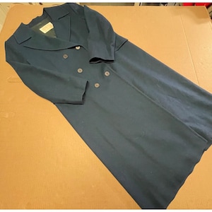 May include: A long, dark navy blue double-breasted coat featuring a wide notched collar, long sleeves, and a series of dark buttons down the front. The interior of the coat displays a visible brand label near the neckline on a dark lining.