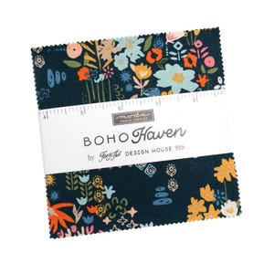 May include: A stack of fabric squares with a dark teal background and a floral pattern in orange, yellow, and blue. The fabric is labeled "BOHO Haven" by Fancy That Design House & Co. A ruler is placed across the top of the fabric squares.