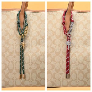 May include: Two decorative bag charms. One is green and white with the name "JENNI" in gold letters, a gold star charm, and gold-toned metal ends. The other is red and white with the name "EMMA" in silver letters and a silver star charm.