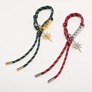 May include: Two rope bracelets, one green and white, the other red and white. Each has a metal accent with the word "DENIM" or "DENIME" and a star-shaped charm. The ends of the ropes are capped with metal.