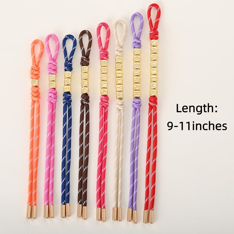 May include: A collection of personalized bracelets in various colors, including orange, pink, blue, brown, red, and purple. Each bracelet features a name spelled out in gold-colored beads. The length of the bracelets is 9-11 inches.
